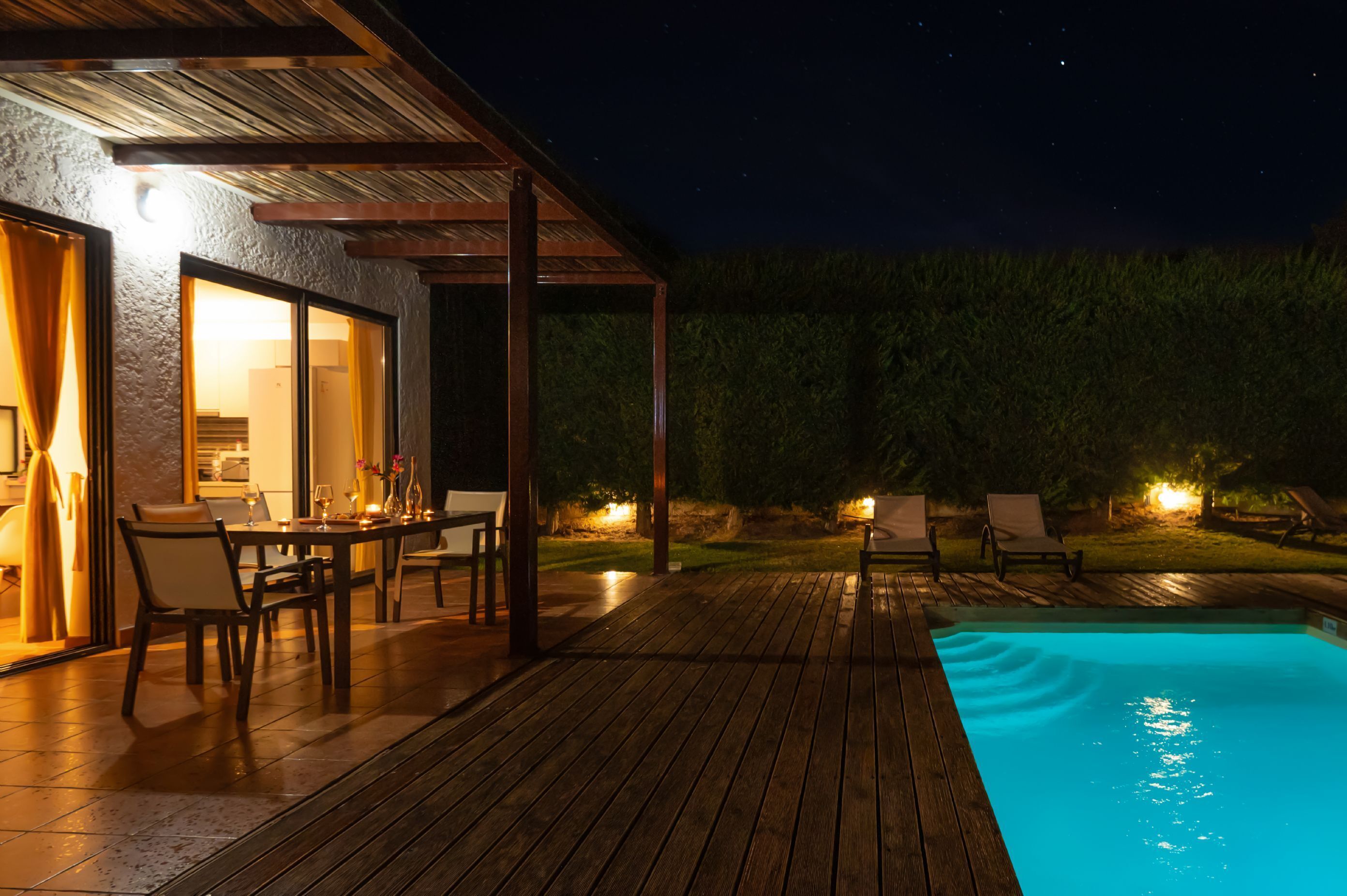 A wooden deck with a pool, outdoor dining area, and lounge chairs.