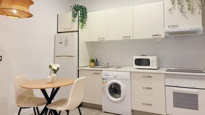 Eine moderne Küche mit weißen Schränken, einer Mikrowelle, einer Waschmaschine und einem Essbereich mit zwei Stühlen und einem Tisch.
