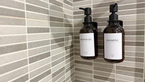 Zwei Flaschen Duschgel und Shampoo an einer gefliesten Wand.