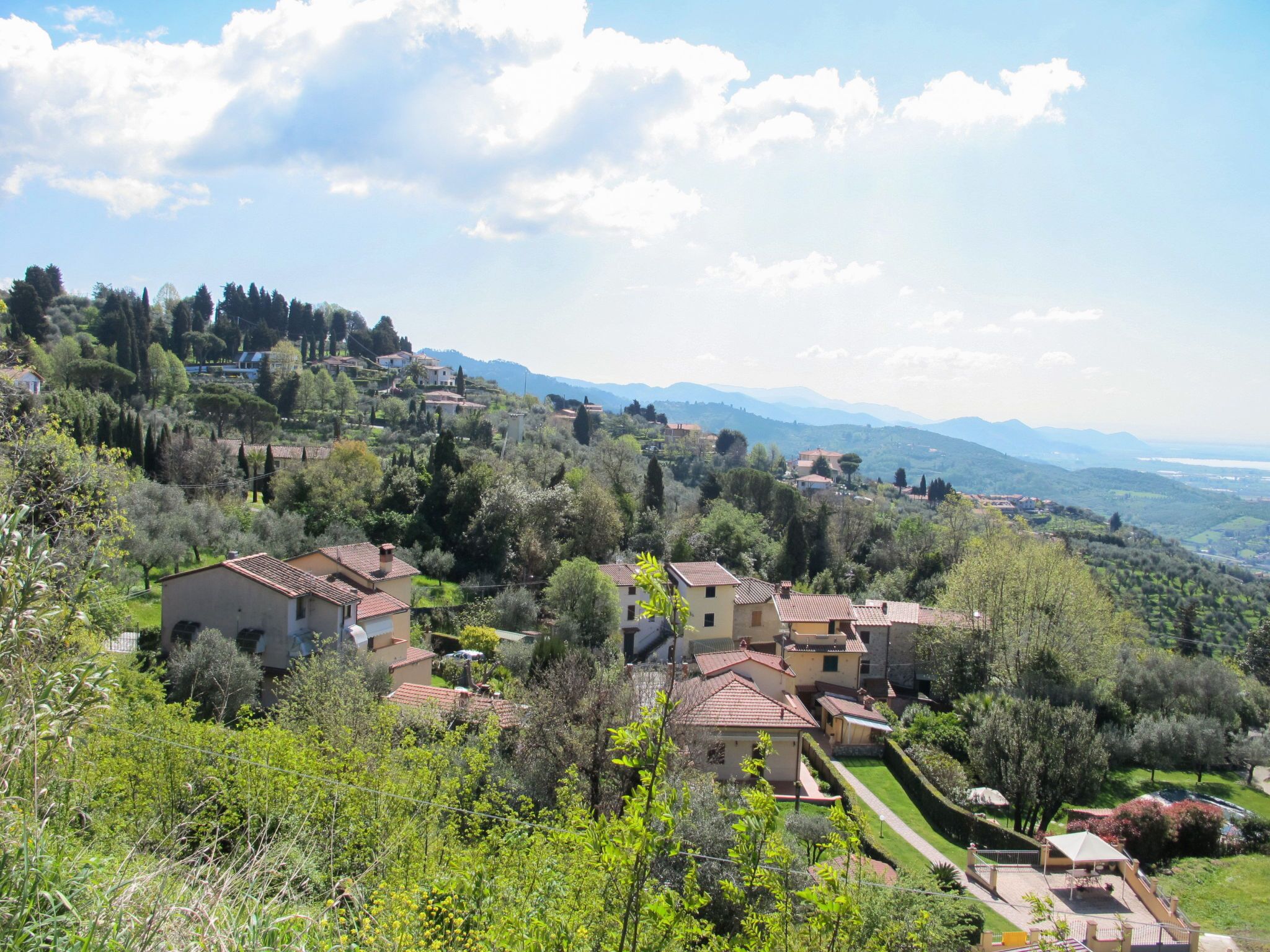 A hillside village with traditional architecture, terraced gardens, and a clear view of distant mountains.