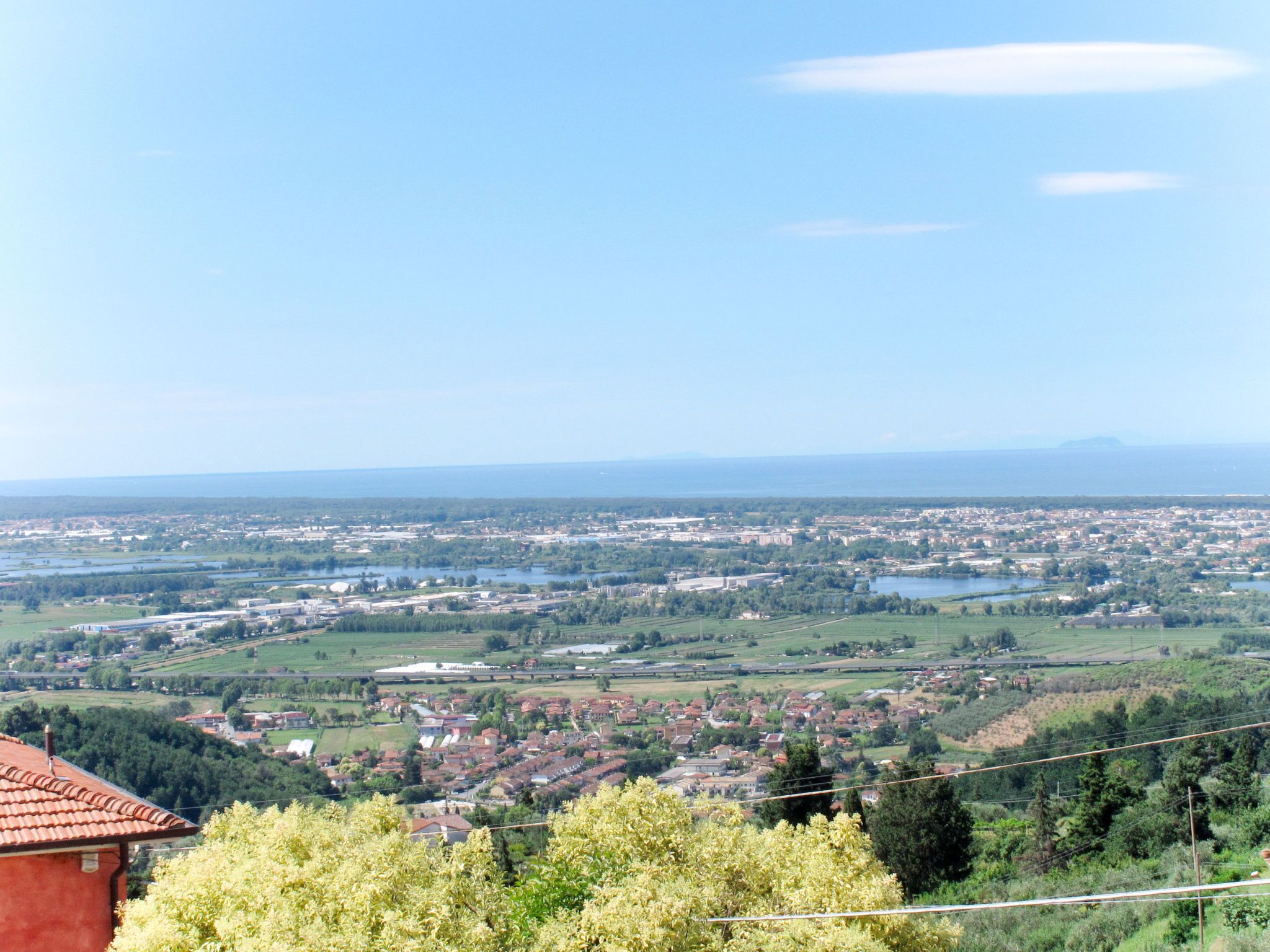 A panoramic view of a coastal town with a mix of residential and commercial buildings, a bridge, and a distant mountain range.