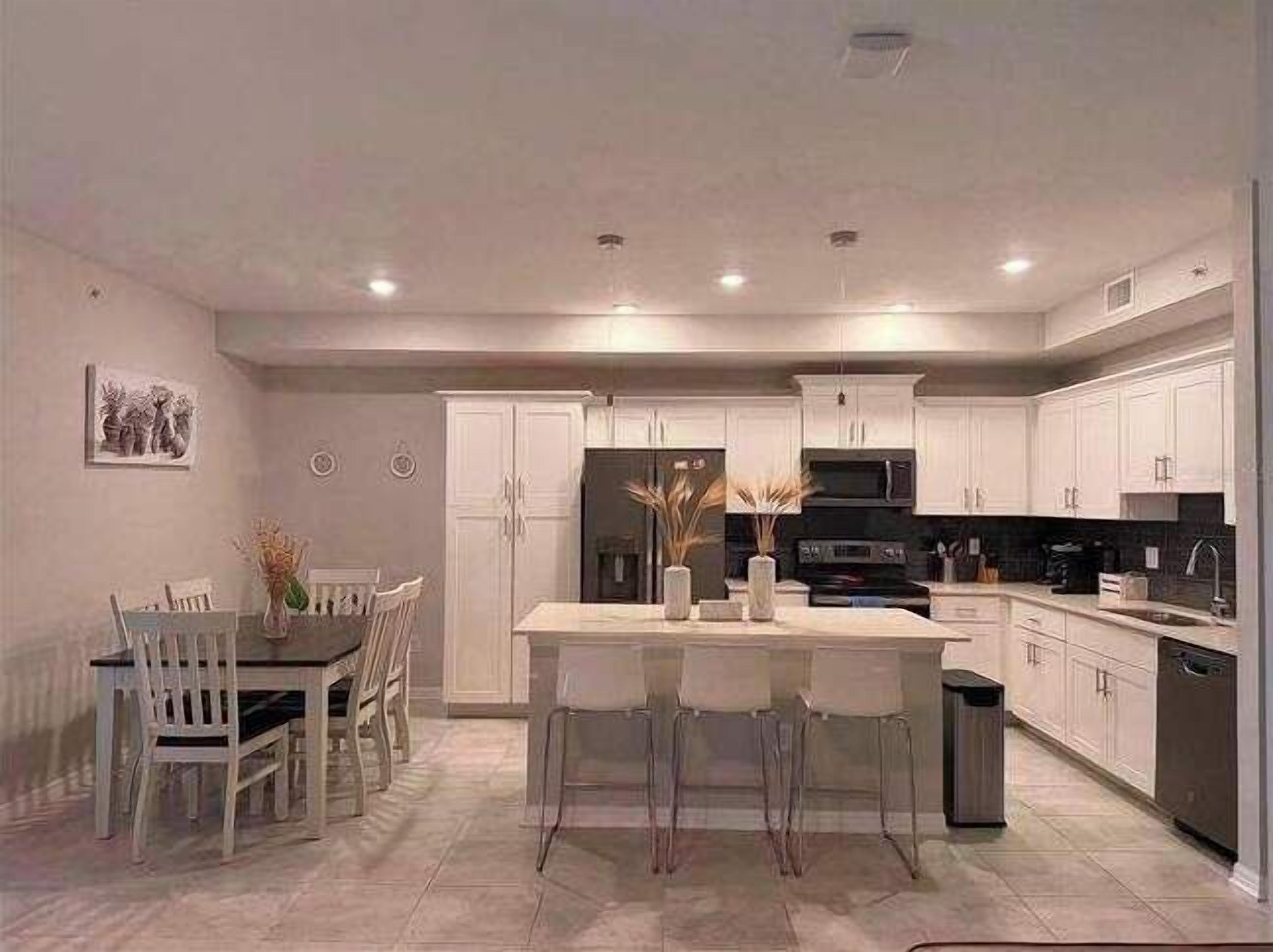A modern kitchen with white cabinetry, a central island, and a dining area with white chairs.