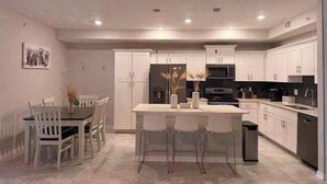 Una cocina moderna con armarios blancos, una isla central y un comedor con sillas blancas.