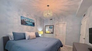 Un dormitorio con una cama grande, una araña, un cuadro y un televisor.
