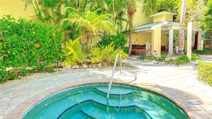 Una piscina con fuente, rodeada de plantas tropicales y un área de terraza cubierta.