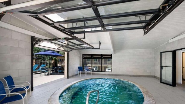 Una piscina interna moderna con tetto in vetro, sedie blu e vista sull'esterno.