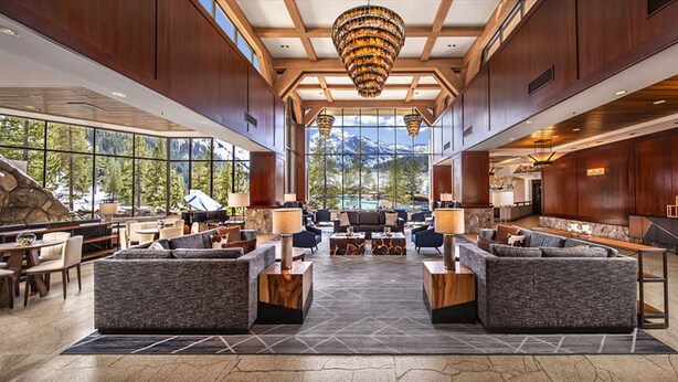 A spacious lobby with a central seating area, large windows offering mountain views, and a stone fireplace. - Everline Resort & Spa Fireplace Suite Forest View (Olympic Valley)