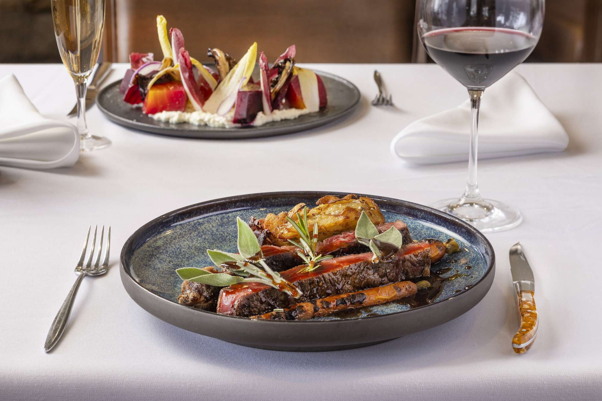 A dining table with a plate of food, a glass of red wine, and a fork.