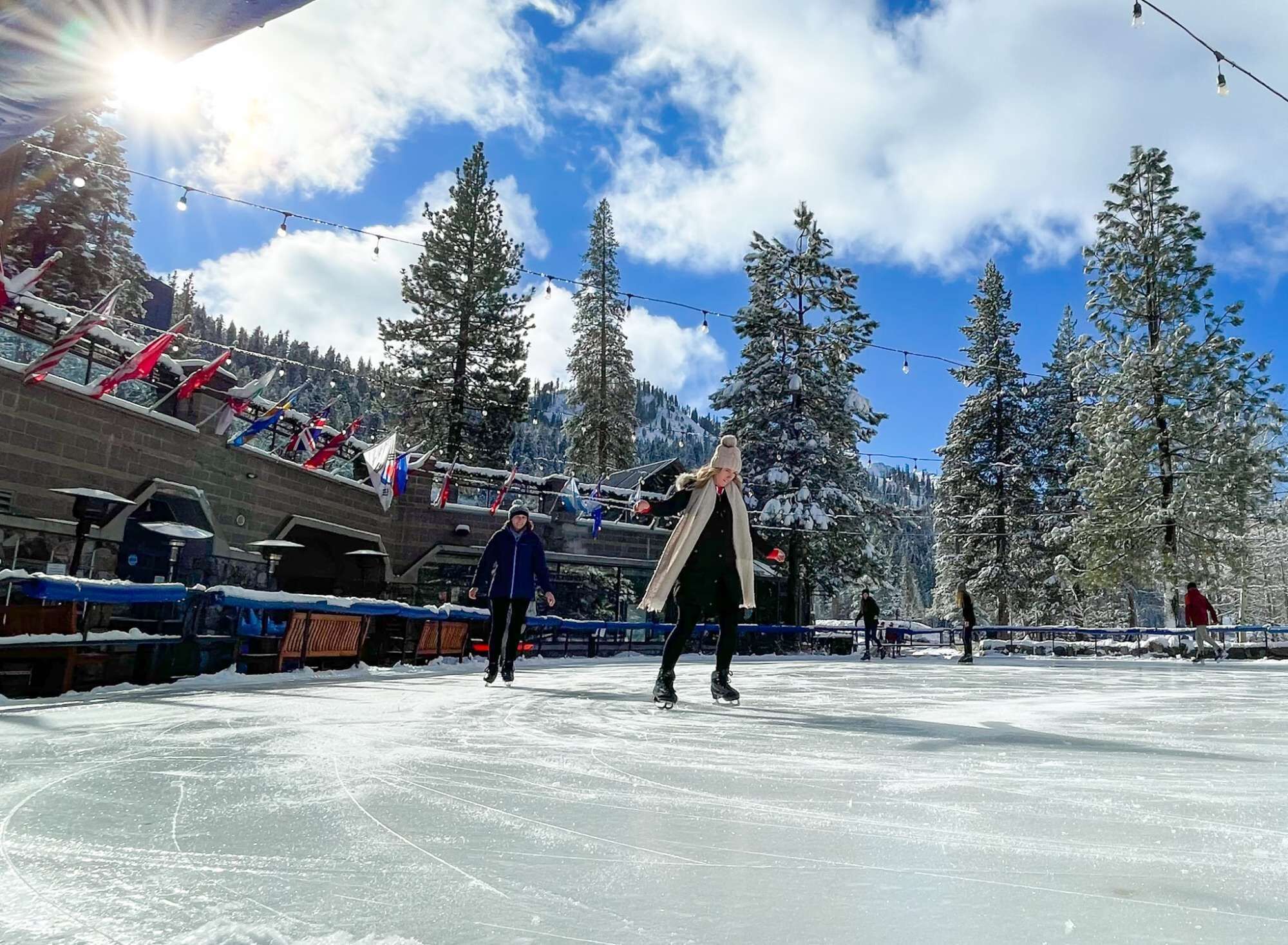 Une patinoire en plein air, avec un ciel dégagé et des arbres enneigés en arrière-plan.