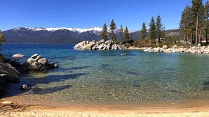 Um lago límpido com margens rochosas e uma praia arenosa.