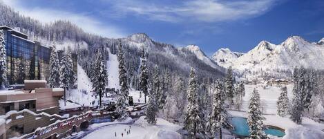 A snow-covered mountain resort with a ski lift, a pool, and a building with large windows.
