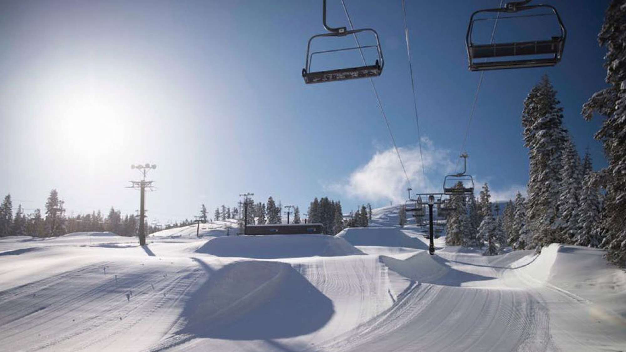 A ski lift chair suspended above a snowy slope with trees in the background.