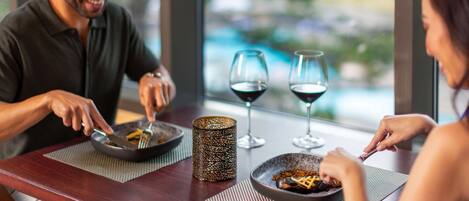 A couple dining at a table with a view of a pool and greenery.