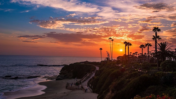 A coastal sunset view with palm trees and a pathway leading to a building.