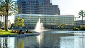 A modern hotel with a large water fountain in the courtyard, surrounded by palm trees and a reflective pond. - Near South Coast Plaza | Pool, Dining + Spa (Santa Ana)
