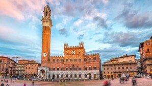 Um edifício histórico com uma torre de relógio imponente e uma grande praça aberta.