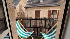 A balcony with two striped hammocks, a wooden floor, and a view of a stone building with a tiled roof. - Duplex apartment in the center of Montignac-Lascaux (Montignac-Lascaux)