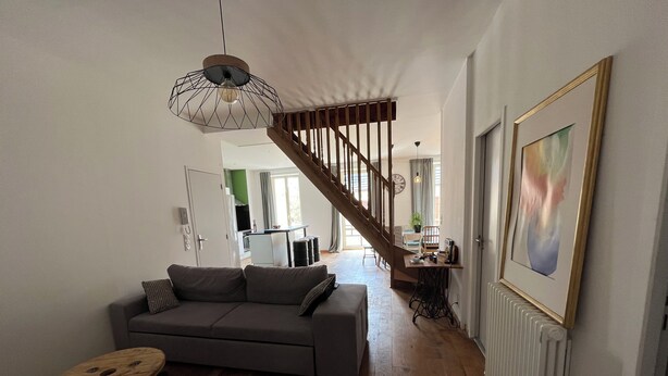 A living room with a sofa, a wooden floor, a staircase, and a dining area in the background. - Duplex apartment in the center of Montignac-Lascaux (Montignac-Lascaux)