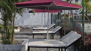 Outdoor seating with a red umbrella, palm trees, and a stone-tiled patio. - SHYAM RESORT (Khandwa)