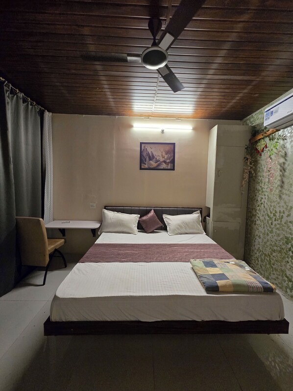 A bedroom with a bed, a desk, a chair, a ceiling fan, and a wall-mounted air conditioner. - SHYAM RESORT (Khandwa)