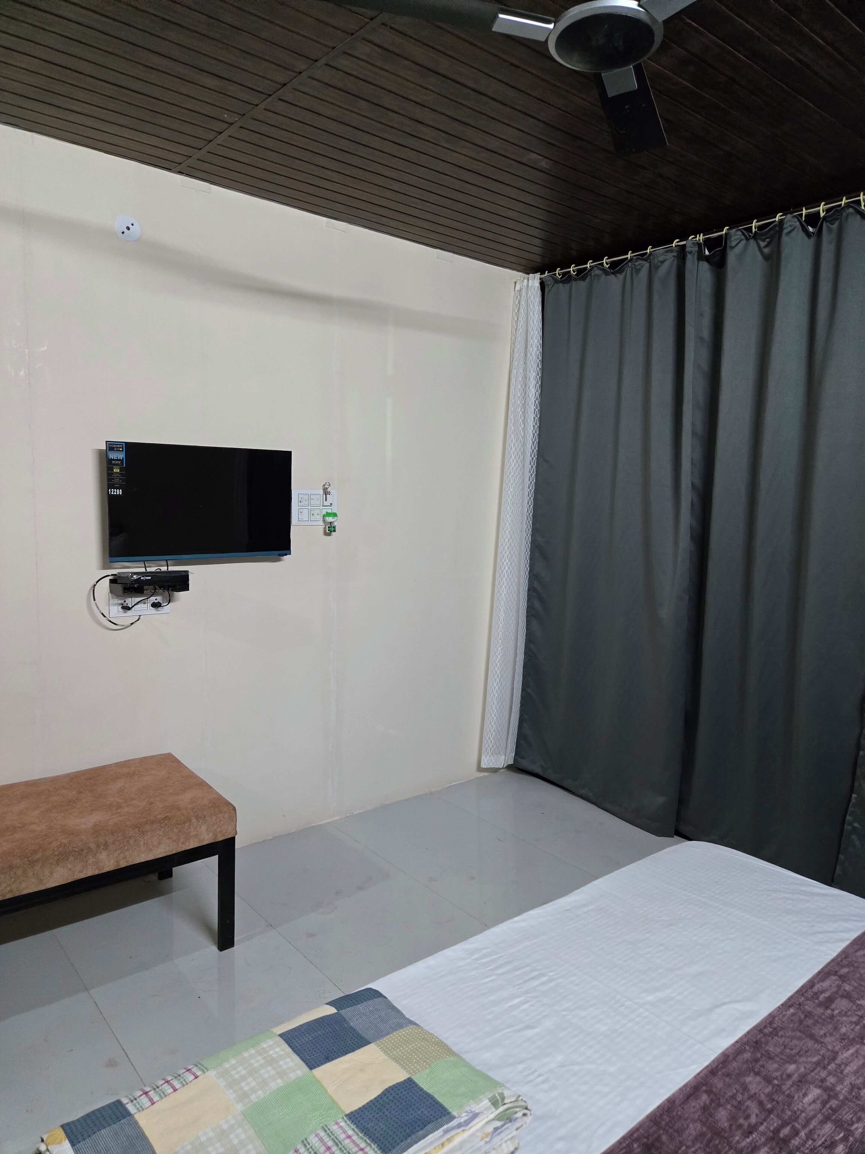 Un dormitorio con cama, un banco, un televisor de pantalla plana montado en la pared y un ventilador de techo.