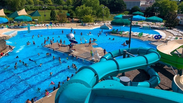 A large outdoor swimming pool with multiple lanes, surrounded by lounge areas and water slides.
