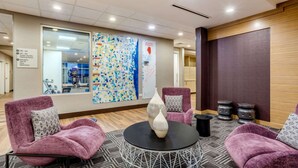 A modern hotel lobby with purple armchairs, a round table with vases, and a large map on the wall.