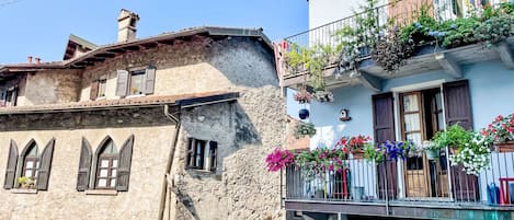 A traditional stone building with arched windows and a balcony with hanging flower baskets.