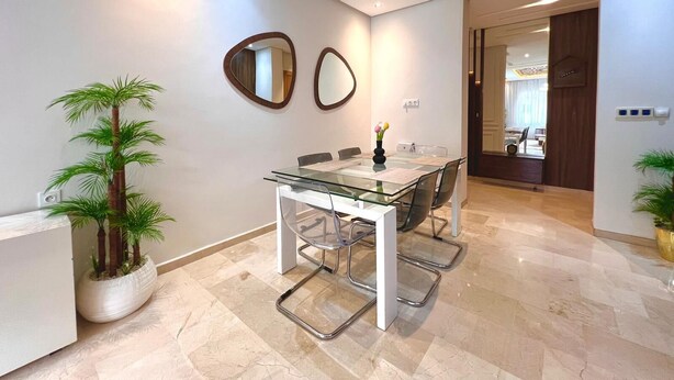 A modern dining area with a glass table and chairs, two wall mirrors, and a potted plant. - 3 bedrooms apartment in secure Résidence (Casablanca)
