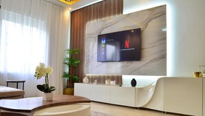 A modern living room with a curved wooden coffee table, a white sofa, a TV mounted on a marble wall, and a potted plant. - 3 bedrooms apartment in secure Résidence (Casablanca)