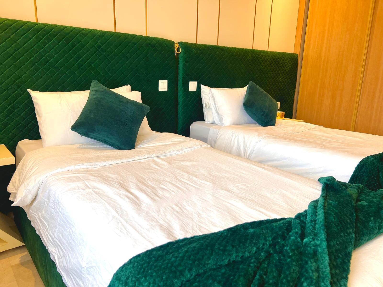A double bed with white linens and green pillows, set against a green upholstered headboard.