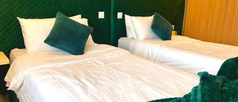 A double bed with white linens and green pillows, set against a green upholstered headboard.