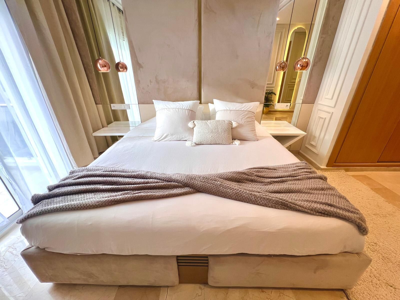 Un dormitorio moderno con una cama grande, ropa de cama blanca y un plaid de punto gris.