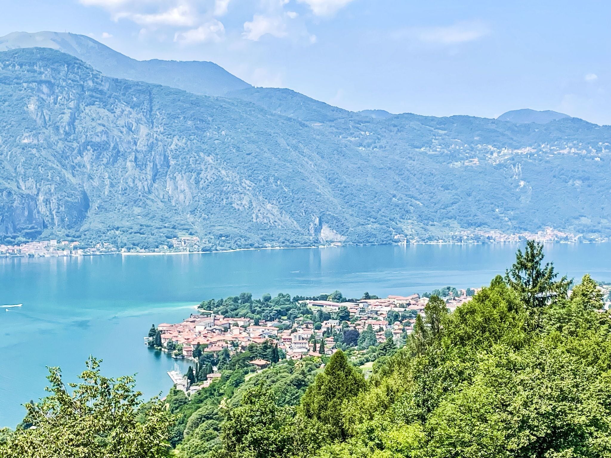 A coastal town with a mountainous backdrop, a clear lake, and dense greenery in the foreground.