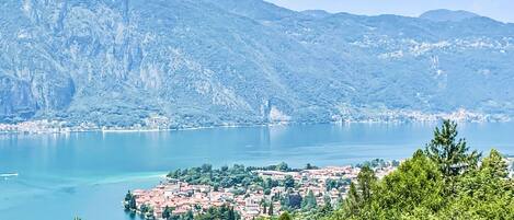 A coastal town with a mountainous backdrop, a clear lake, and dense greenery in the foreground.