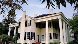 A large, two-story house with a wrap-around porch supported by columns, featuring a symmetrical facade with evenly spaced windows and a central entrance. - Suite w/ Kitchen + Free Parking & Outdoor Pool (Florence)