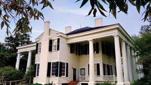 A large, two-story house with a wrap-around porch supported by columns, featuring a symmetrical facade with evenly spaced windows and a central entrance. - 2 Bedroom Suite w/ Kitchen + Free Parking & Pool (Florence)