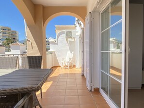 A balcony with a wicker table and chairs, a sliding glass door, and a view of buildings in the background. - Apartment in Nerja Near Burriana Beach (Nerja)