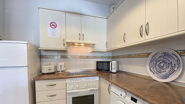 A compact kitchen with white cabinets, a microwave, a toaster, a washing machine, and a coffee maker. - Apartment in Nerja Near Burriana Beach (Nerja)