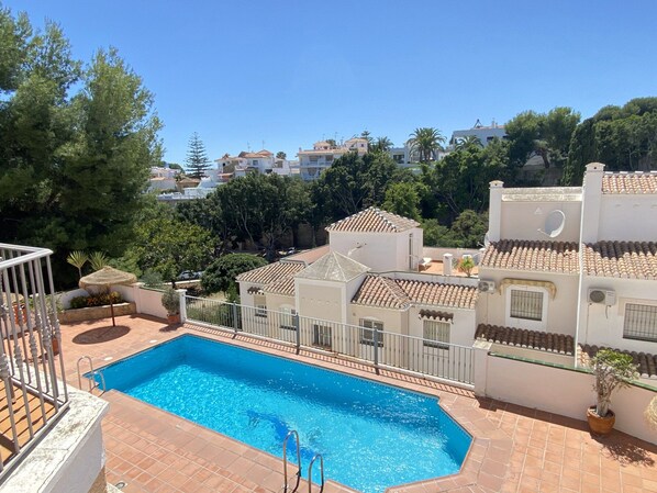 A swimming pool with a tiled deck, surrounded by buildings with terracotta roofs and white walls. - Apartment in Nerja Near Burriana Beach (Nerja)