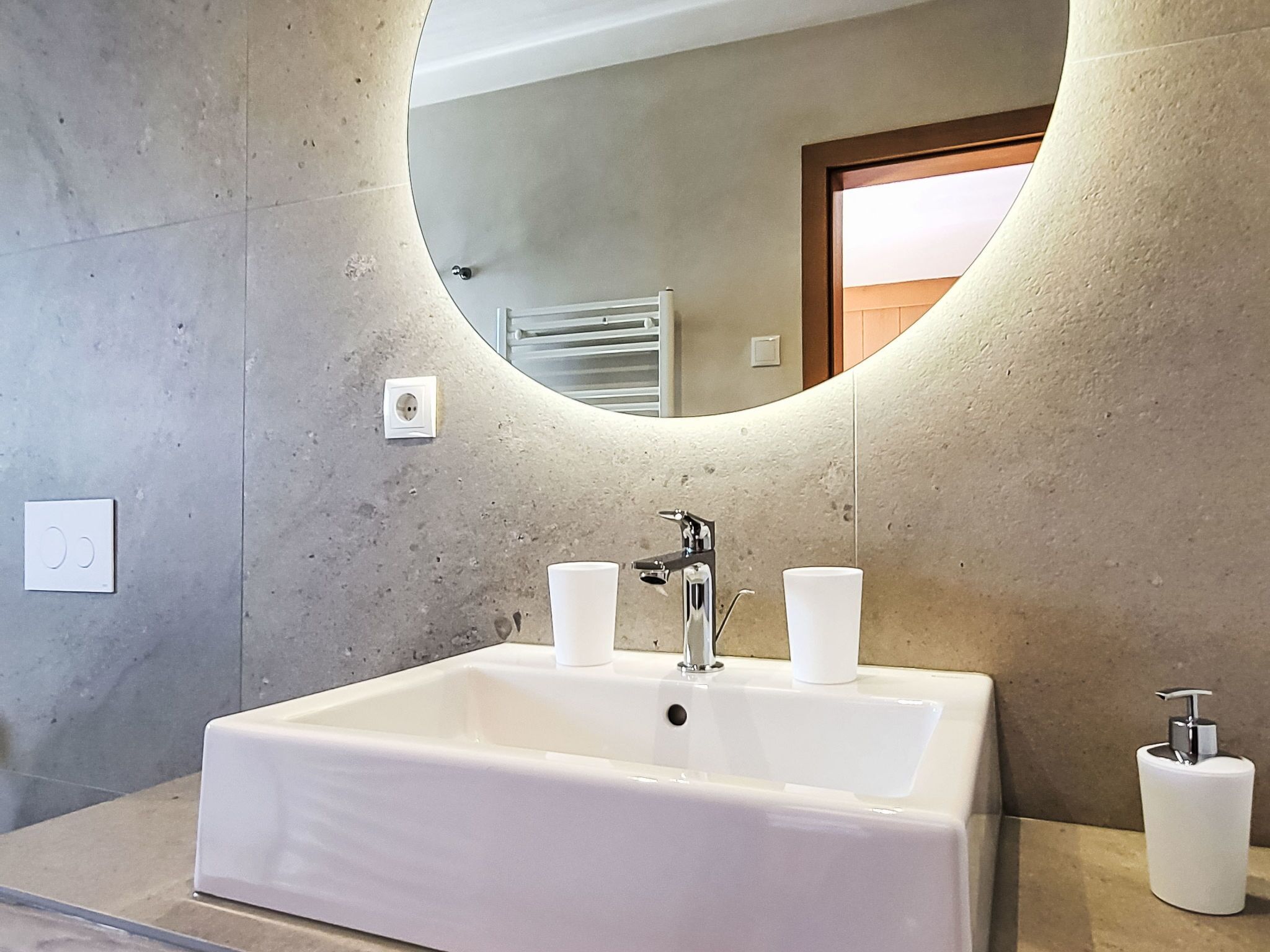 A bathroom with a large oval mirror, a white sink with two faucets, and a toilet paper holder.