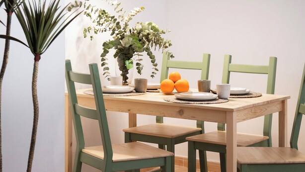 Een eetgedeelte met een houten tafel, groene stoelen en hangende hanglampen.