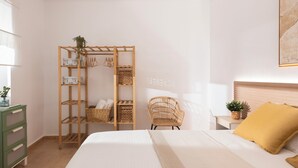 Een slaapkamer met een bed, een houten plankkast, een rieten stoel en een nachtkastje met een plant.