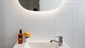 Een badkamer met een witte wastafel, een ronde spiegel met verlichting en een zeepfles.