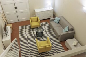 Uma sala de estar com um sofá, duas poltronas amarelas, uma mesa de centro, um tapete estampado, um aparador branco e um abajur.