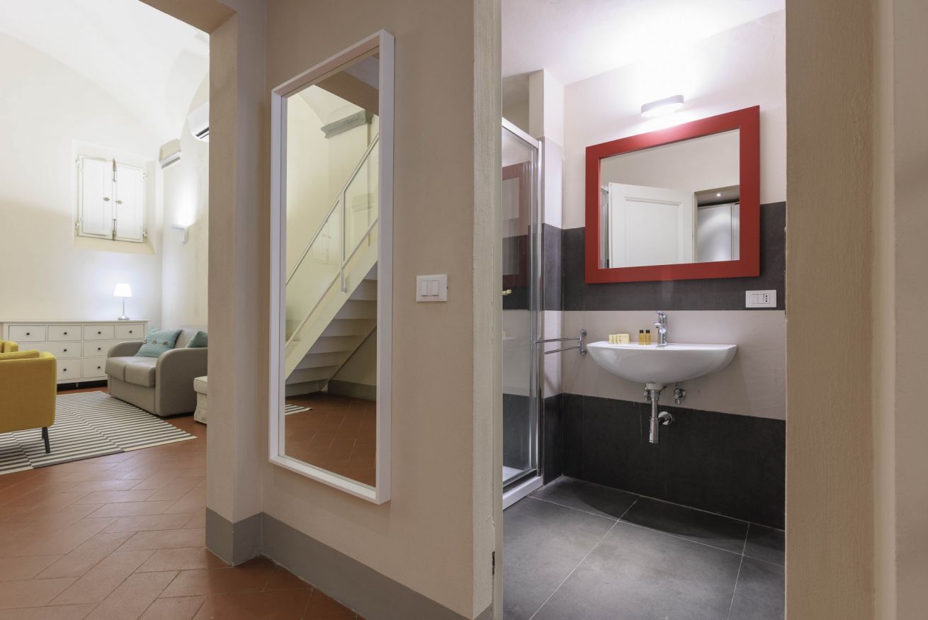 A modern bathroom with a glass shower, a white sink, and a red-framed mirror.