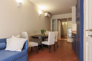 A dining area with a round table, white chairs, a blue sofa, and a potted plant. - Santa Croce Deluxe Apartment (Firenze)