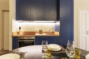 A modern kitchen with dark blue cabinets, a wooden countertop, and a dining area with a table set for two. - Santa Croce Deluxe Apartment (Firenze)