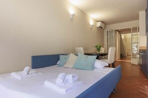 A neatly made bed with pillows and towels, a small table with a vase, and a chair. - Santa Croce Deluxe Apartment (Firenze)