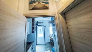 Un pasillo con un cuadro de un faro, una lámpara de pared y una puerta que da a un comedor.